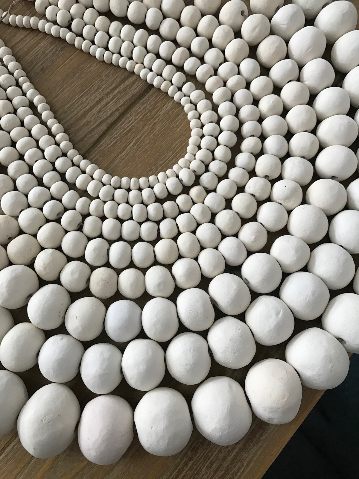 Multiple strands of clay beads arranged in curved rows on a brown wooden surface.